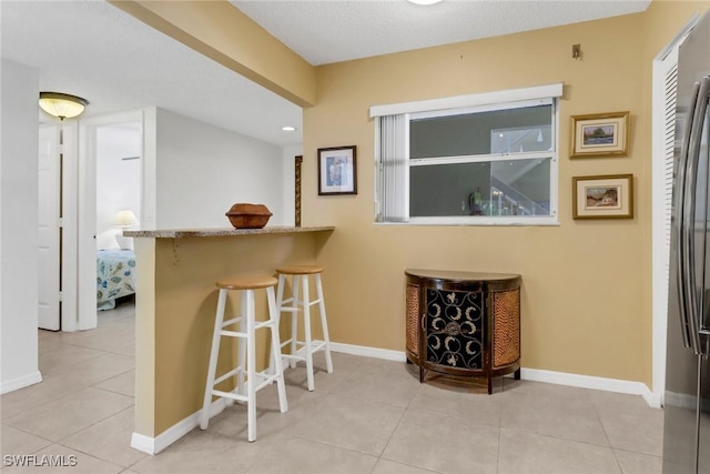 interior space featuring a breakfast bar, stainless steel fridge, kitchen peninsula, and light tile patterned flooring