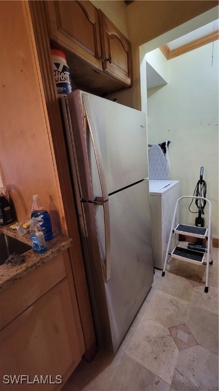 kitchen featuring ornamental molding, stainless steel refrigerator, stone countertops, and washer / dryer