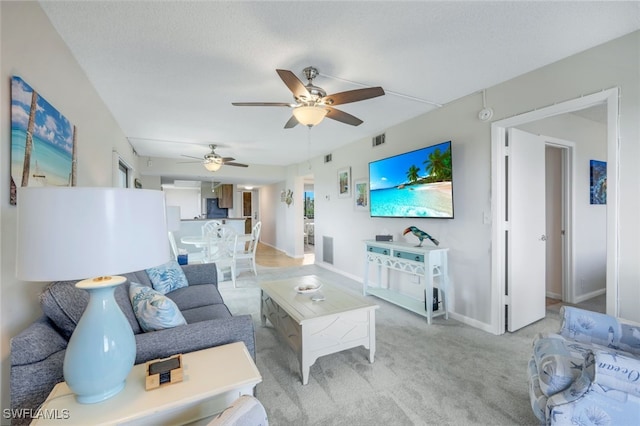 living room with a textured ceiling, ceiling fan, and light colored carpet