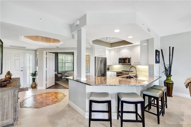 kitchen featuring white cabinets, a raised ceiling, kitchen peninsula, stainless steel appliances, and light stone countertops