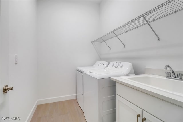 laundry area with separate washer and dryer, sink, light hardwood / wood-style flooring, and cabinets