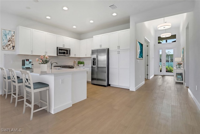 kitchen featuring white cabinets, french doors, decorative light fixtures, stainless steel appliances, and light hardwood / wood-style floors