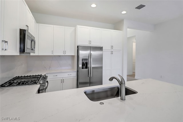 kitchen with light stone counters, sink, white cabinets, decorative backsplash, and appliances with stainless steel finishes