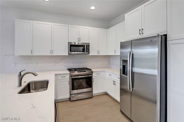 kitchen with white cabinets, sink, tasteful backsplash, stainless steel appliances, and light wood-type flooring