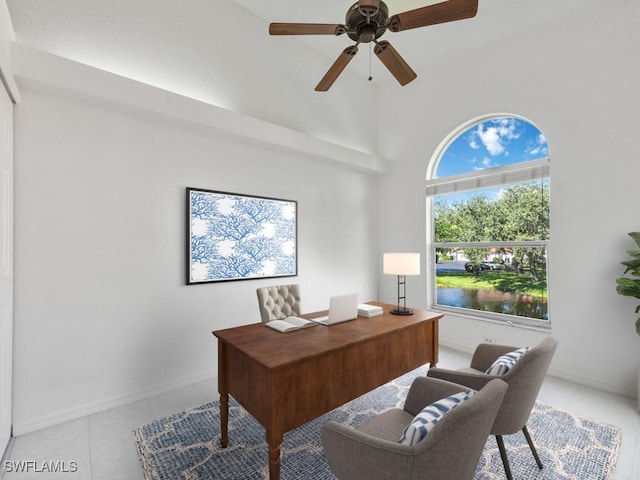 tiled home office with ceiling fan, a towering ceiling, and a water view