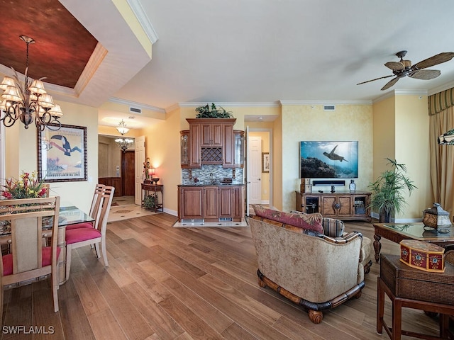 living room with ceiling fan with notable chandelier, hardwood / wood-style flooring, and ornamental molding