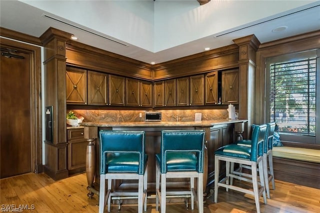 kitchen featuring a kitchen breakfast bar, light stone countertops, light wood-type flooring, tasteful backsplash, and dark brown cabinets