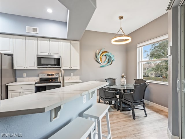 kitchen with white cabinets, hanging light fixtures, light hardwood / wood-style flooring, stainless steel appliances, and light stone countertops