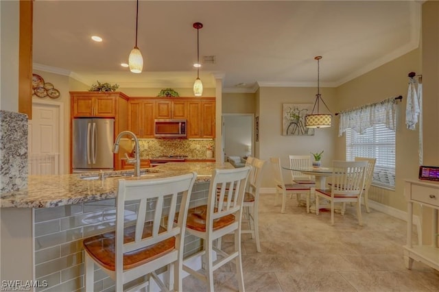 kitchen featuring light stone countertops, stainless steel appliances, ornamental molding, and a breakfast bar area