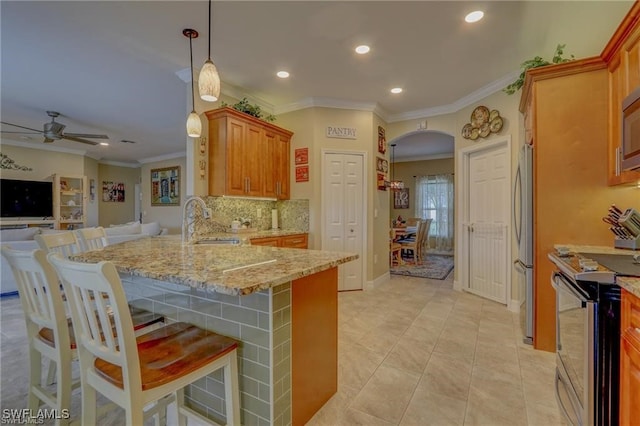 kitchen with a breakfast bar, kitchen peninsula, stainless steel appliances, light stone countertops, and ceiling fan