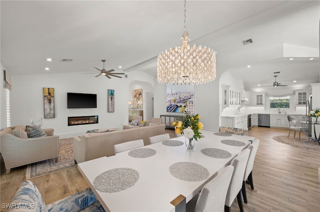 dining area featuring ceiling fan with notable chandelier, vaulted ceiling, sink, and light wood-type flooring