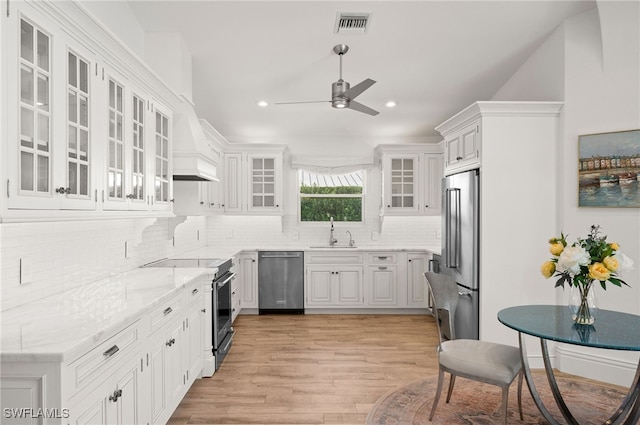 kitchen featuring custom exhaust hood, white cabinets, appliances with stainless steel finishes, and light hardwood / wood-style flooring