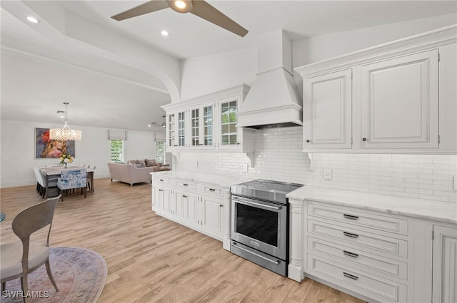 kitchen featuring white cabinets, custom exhaust hood, tasteful backsplash, stainless steel range with electric stovetop, and light wood-type flooring