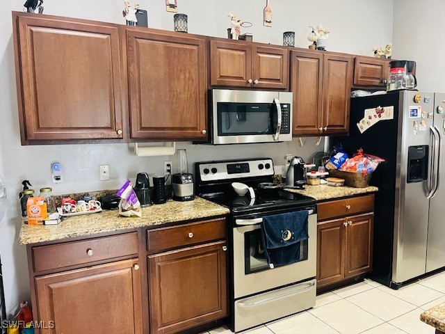 kitchen with appliances with stainless steel finishes, light tile patterned flooring, and light stone counters