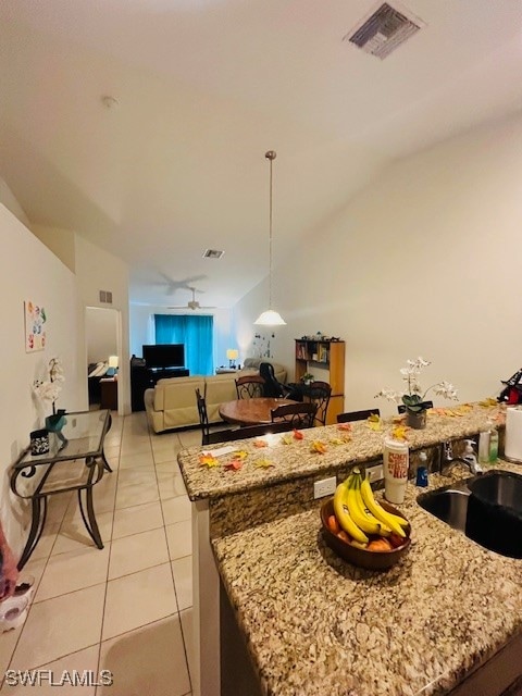 kitchen with a kitchen island, sink, light stone countertops, light tile patterned floors, and ceiling fan