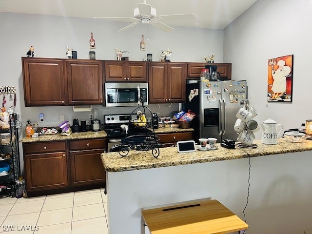 kitchen featuring dark brown cabinets, ceiling fan, stainless steel appliances, light stone counters, and light tile patterned floors