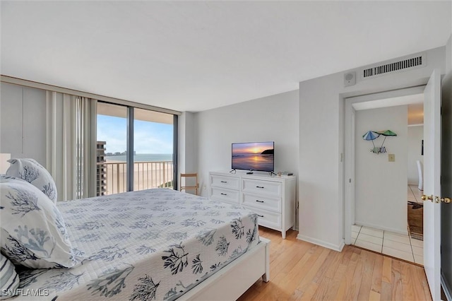 bedroom featuring visible vents, baseboards, access to outside, light wood-style floors, and floor to ceiling windows