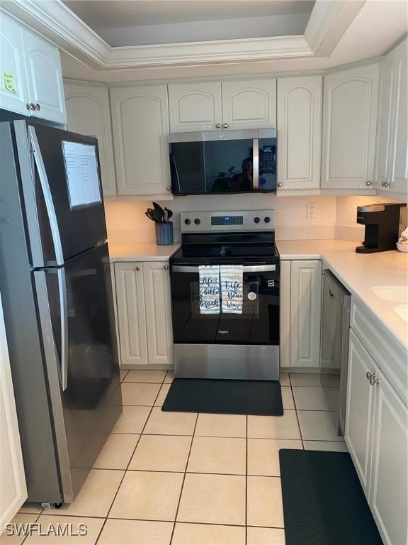 kitchen featuring light tile patterned floors, white cabinetry, light countertops, appliances with stainless steel finishes, and crown molding