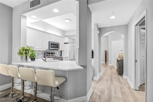 kitchen featuring appliances with stainless steel finishes, a kitchen breakfast bar, white cabinets, kitchen peninsula, and light hardwood / wood-style flooring