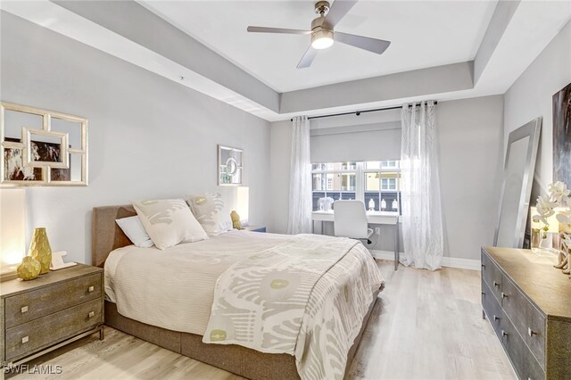 bedroom featuring light hardwood / wood-style flooring, ceiling fan, and a raised ceiling