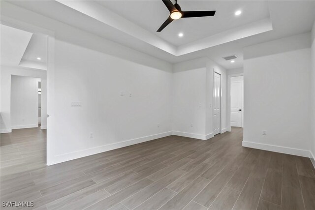 unfurnished room featuring ceiling fan, a tray ceiling, and light hardwood / wood-style floors