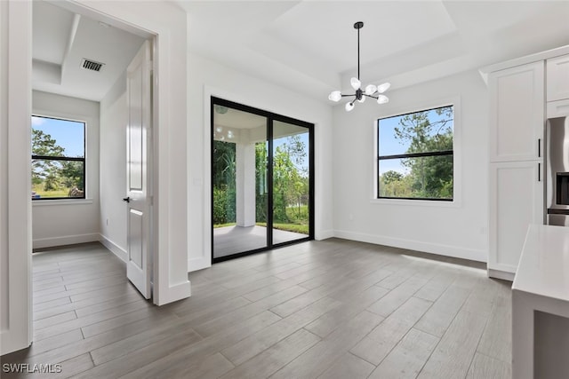 unfurnished room featuring an inviting chandelier, light hardwood / wood-style floors, a raised ceiling, and a healthy amount of sunlight