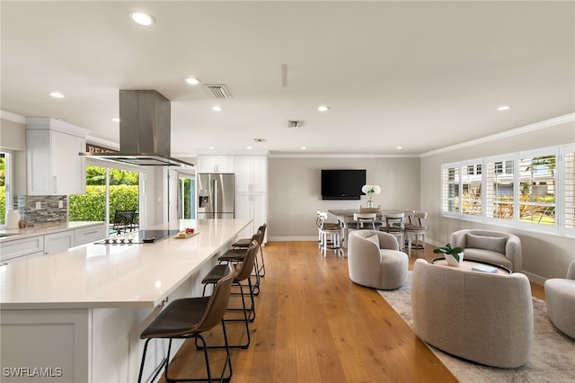 kitchen featuring stainless steel refrigerator with ice dispenser, a healthy amount of sunlight, range hood, white cabinets, and black stovetop