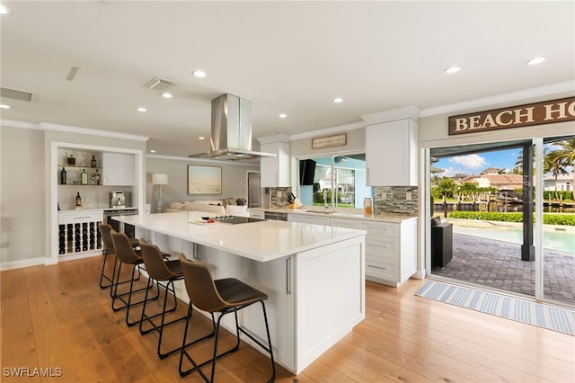 kitchen with light hardwood / wood-style floors, a kitchen bar, white cabinetry, and range hood