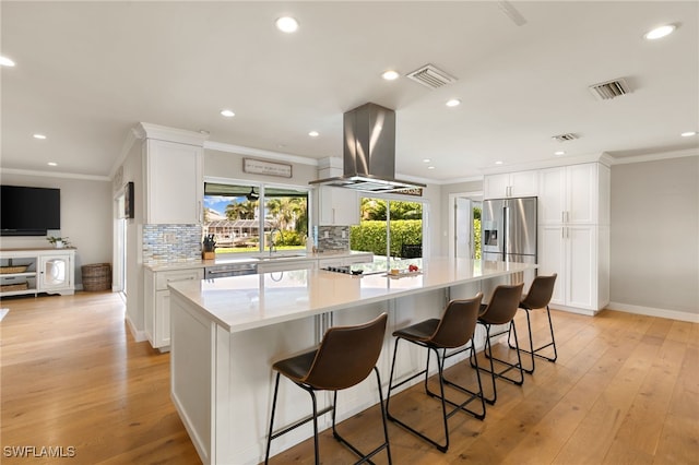 kitchen with white cabinets, decorative backsplash, light wood-type flooring, a large island, and island range hood