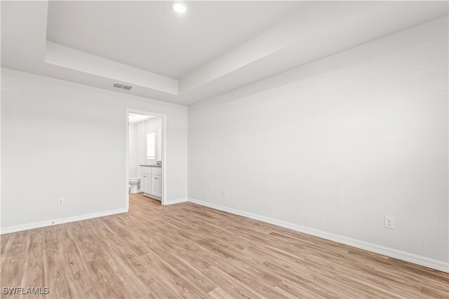 empty room with a raised ceiling and light hardwood / wood-style flooring