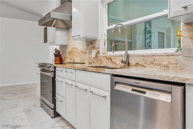 kitchen with light stone counters, sink, wall chimney range hood, white cabinetry, and appliances with stainless steel finishes