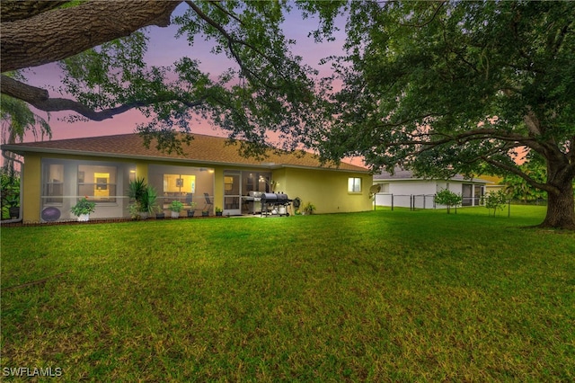 back house at dusk featuring a yard and a patio area