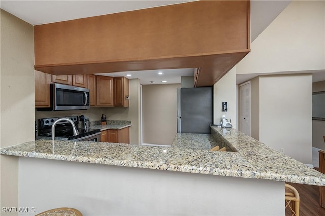 kitchen featuring a kitchen breakfast bar, light stone counters, kitchen peninsula, and stainless steel appliances