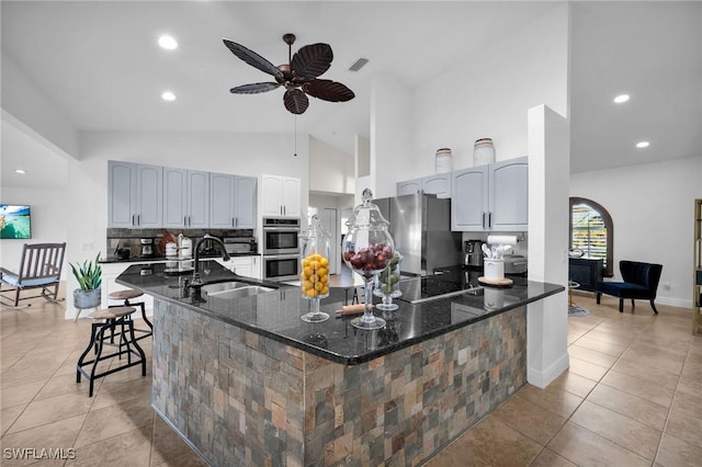 kitchen with a breakfast bar area, appliances with stainless steel finishes, a sink, ceiling fan, and dark stone countertops