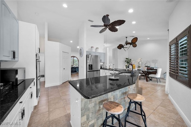 kitchen featuring a center island, stainless steel appliances, white cabinetry, a sink, and a kitchen bar