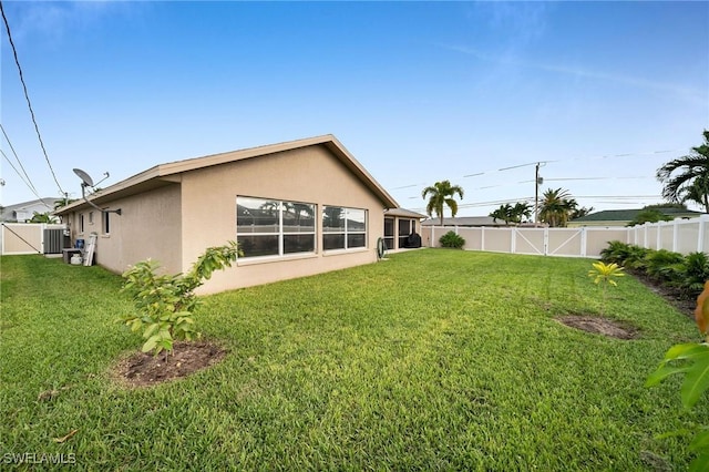 back of property with a yard, central AC unit, a fenced backyard, and stucco siding