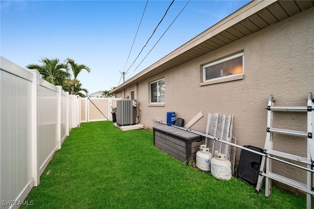 view of yard with central AC unit, a fenced backyard, and a gate