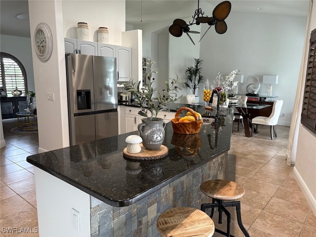 kitchen with light tile patterned floors, stainless steel fridge, white cabinets, dark stone countertops, and a kitchen bar