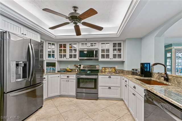 kitchen featuring white cabinets, light stone counters, appliances with stainless steel finishes, a tray ceiling, and sink