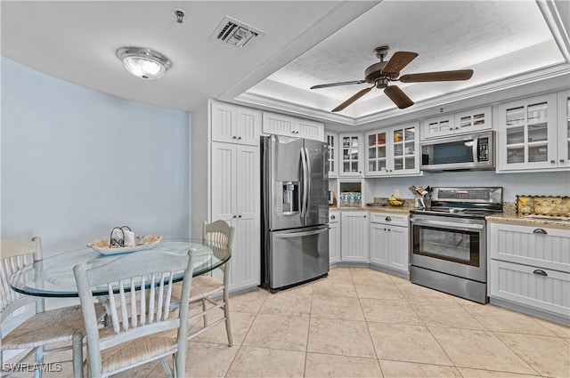 kitchen featuring appliances with stainless steel finishes, white cabinetry, a tray ceiling, light tile patterned flooring, and light stone counters