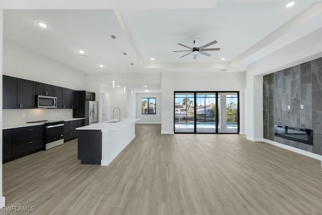 kitchen featuring appliances with stainless steel finishes, sink, an island with sink, light hardwood / wood-style floors, and pendant lighting