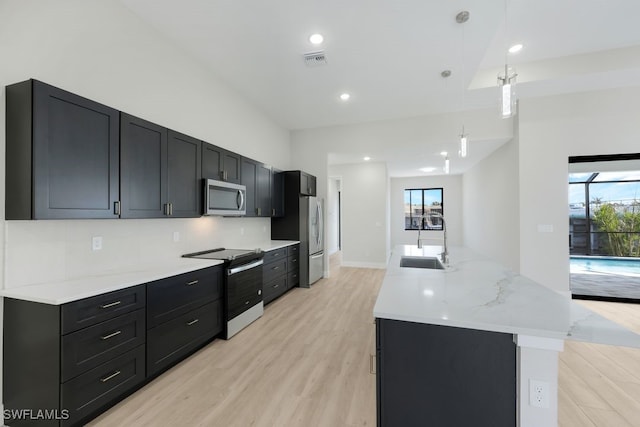 kitchen with stainless steel appliances, hanging light fixtures, sink, and light wood-type flooring