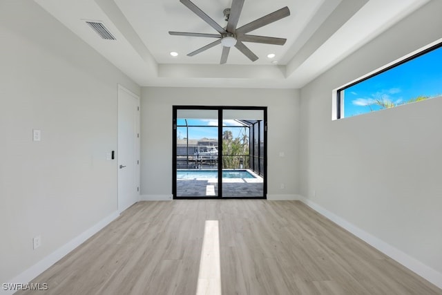 unfurnished room featuring light hardwood / wood-style floors, a tray ceiling, plenty of natural light, and ceiling fan