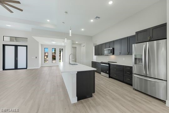 kitchen featuring an island with sink, stainless steel appliances, sink, pendant lighting, and light hardwood / wood-style floors