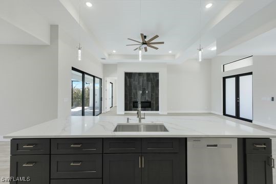 kitchen with a tray ceiling, sink, stainless steel dishwasher, light stone counters, and ceiling fan