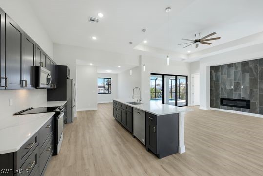 kitchen with stainless steel appliances, a tile fireplace, a center island with sink, sink, and light wood-type flooring