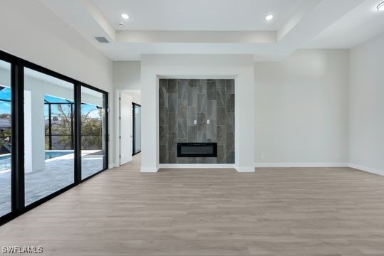 unfurnished living room featuring a tile fireplace, light wood-type flooring, and a raised ceiling