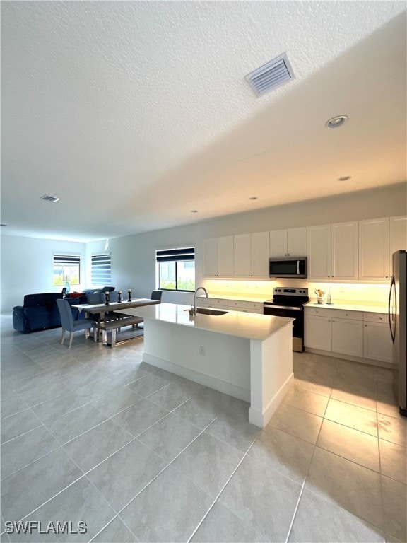 kitchen featuring white cabinetry, sink, a kitchen island with sink, light tile patterned floors, and appliances with stainless steel finishes