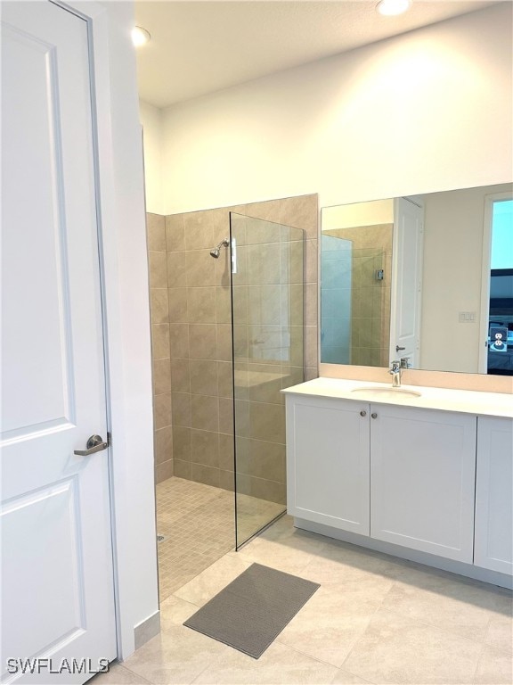 bathroom with tile patterned flooring, a tile shower, and vanity