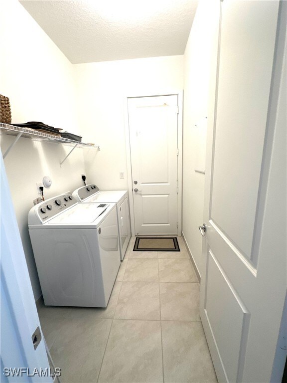 clothes washing area with light tile patterned flooring, washing machine and dryer, and a textured ceiling